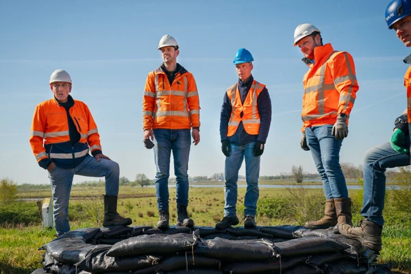 projectleden die op een muur van zandzakken staan